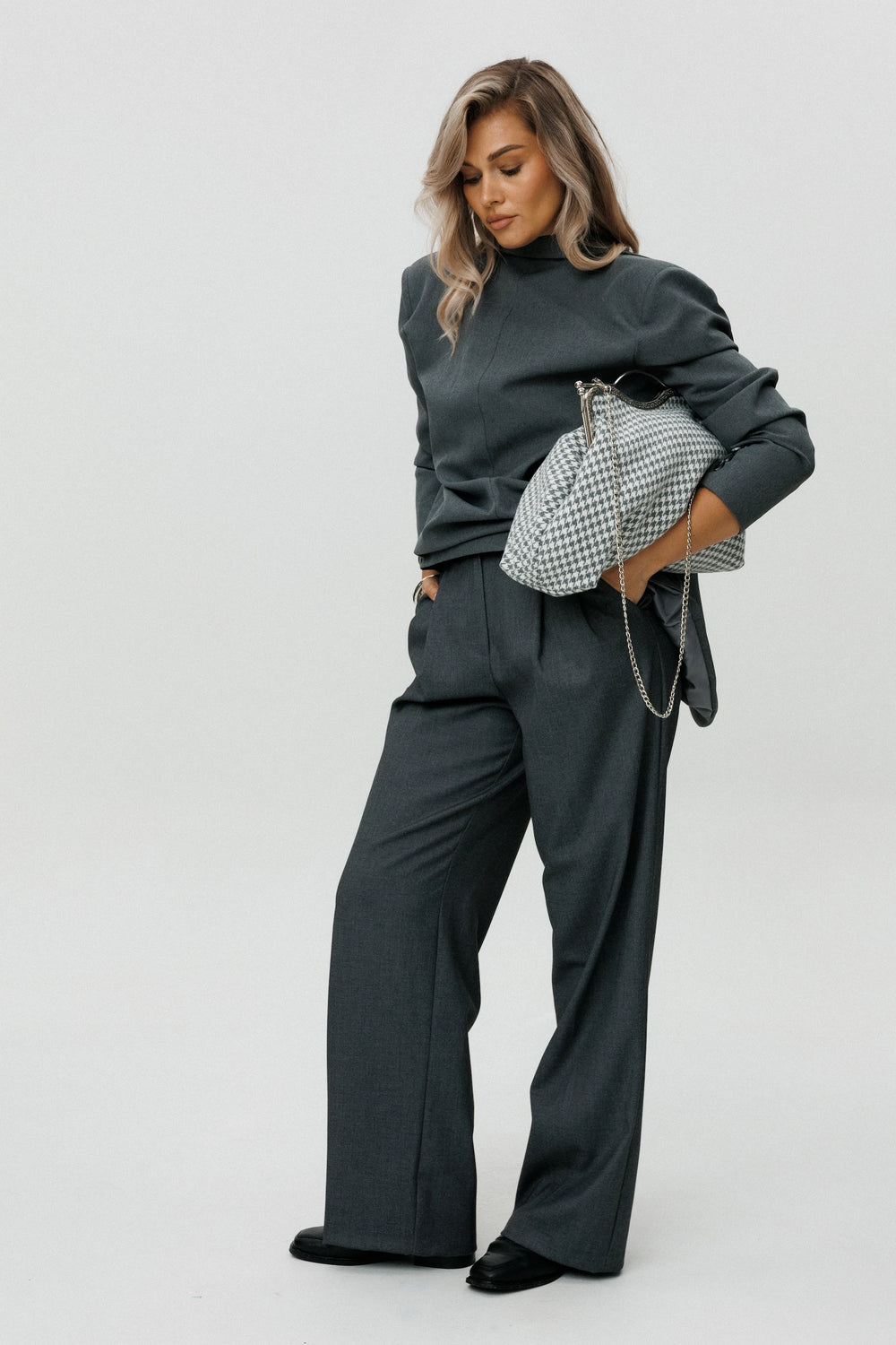 Woman wearing a dark gray outfit with a checkered handbag on a white background