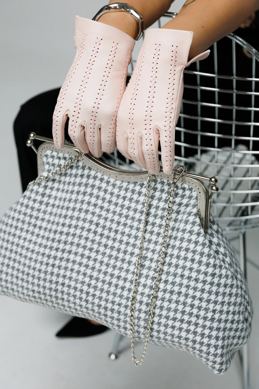 Person wearing pink gloves holding a houndstooth patterned handbag.