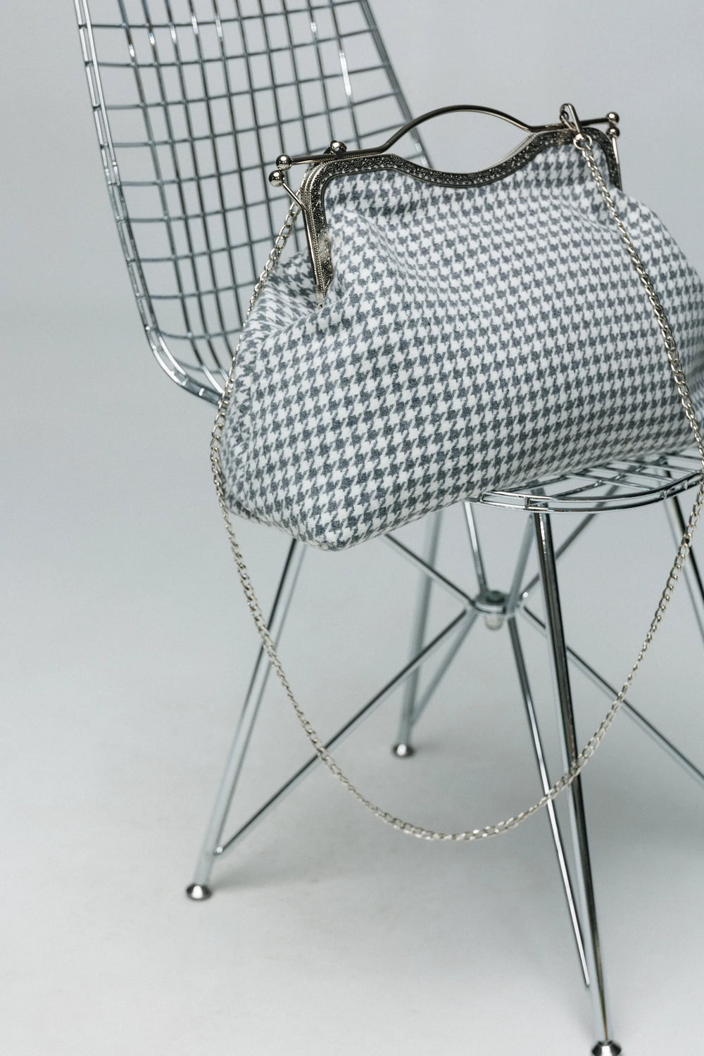 Houndstooth patterned handbag with chain detail on a metal chair against a light background