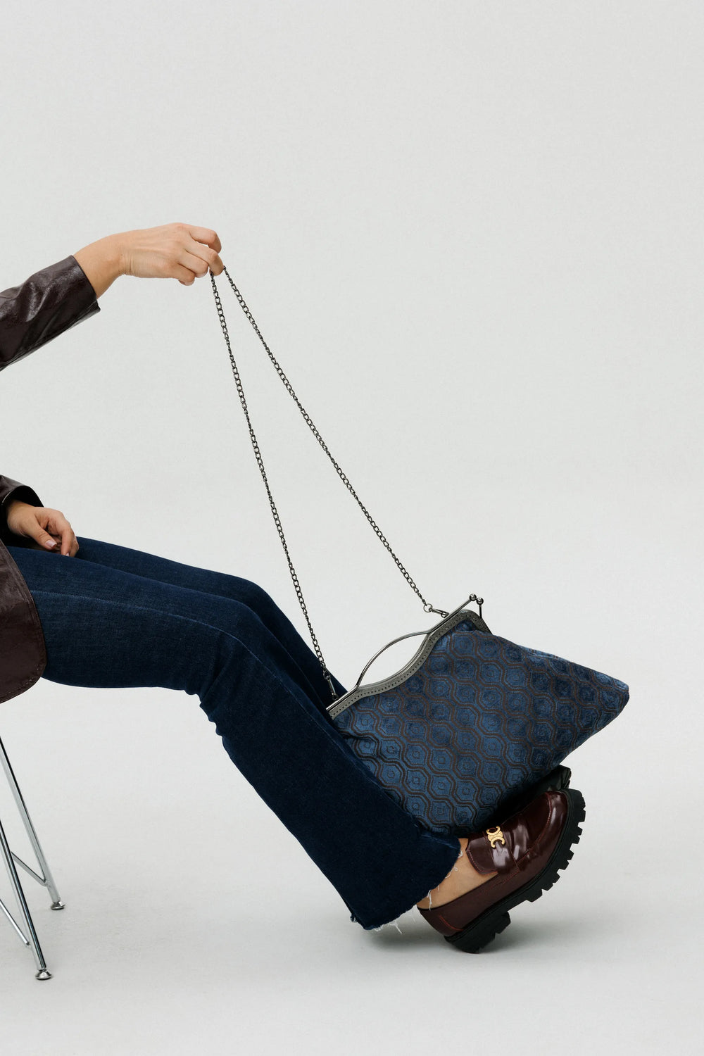 Person sitting on a chair holding a blue patterned handbag with a chain strap.