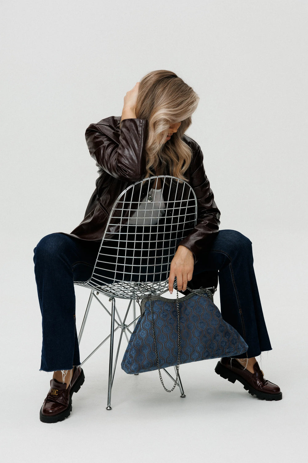 Person sitting on a wire chair holding a blue handbag against a white background