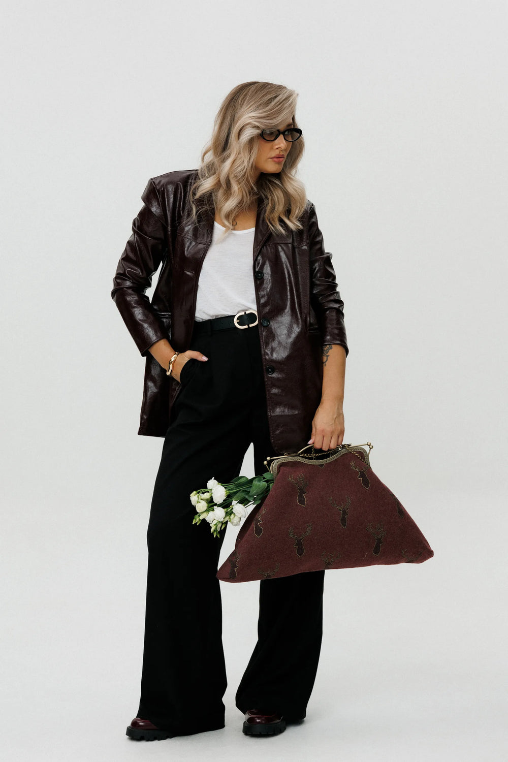 Woman in leather jacket and black pants holding a matching handbag against a white background