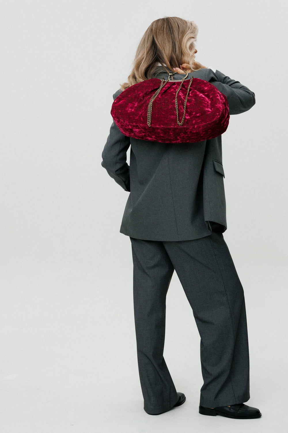 Person wearing a gray suit holding a red velvet bag on a white background