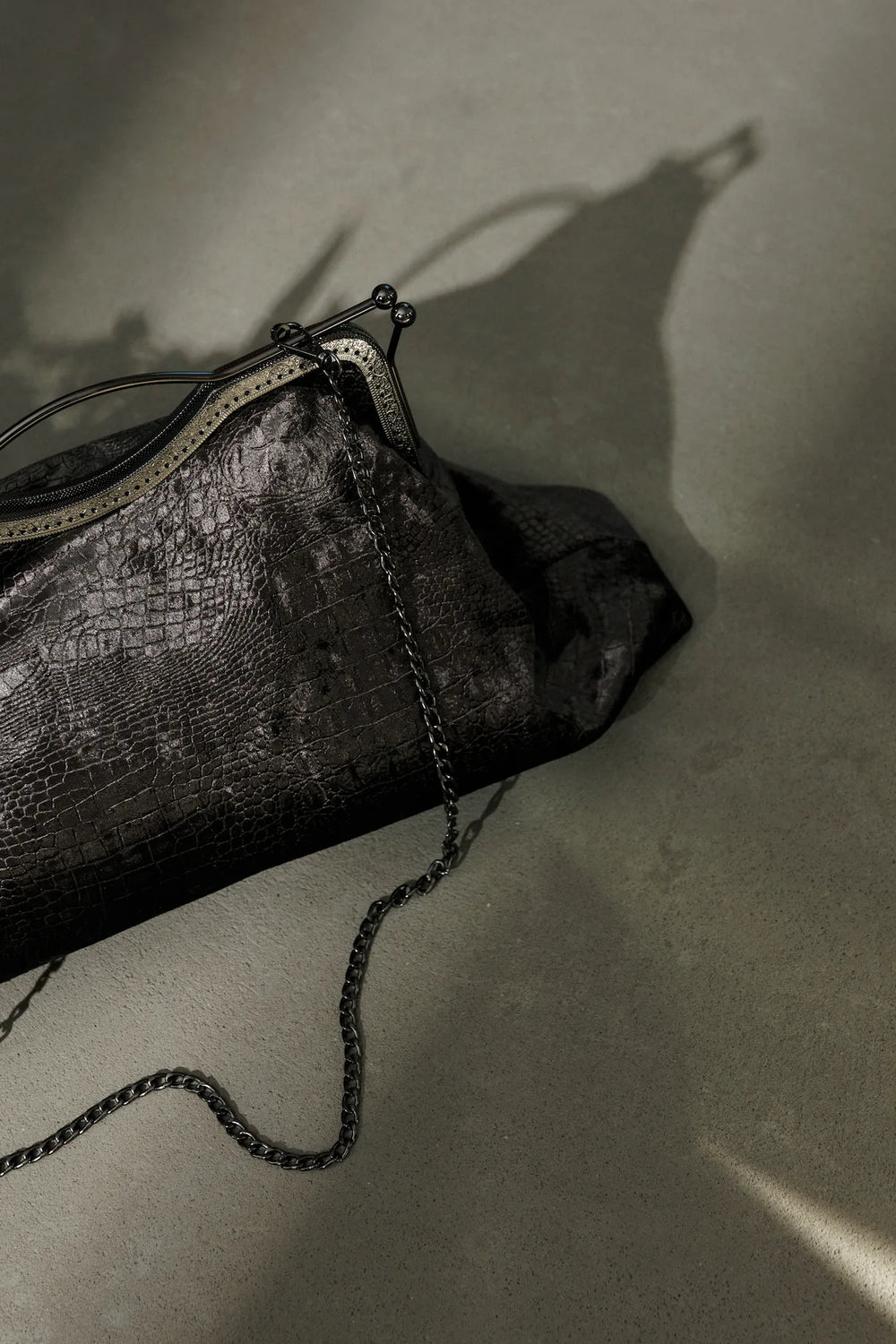 Black textured clutch bag with chain detail on a gray surface