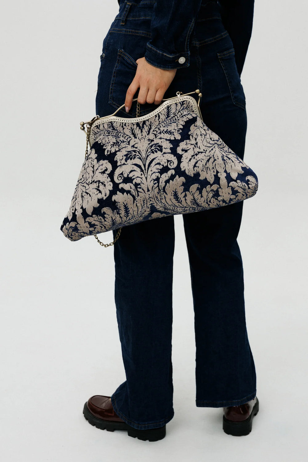 Person holding a decorative clutch bag with a floral pattern on a white background