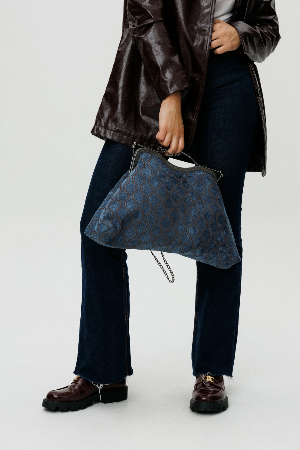 Person holding a blue patterned handbag against a white background