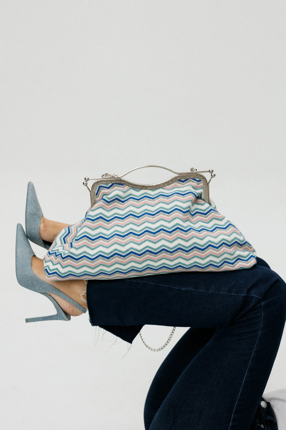 Person wearing high heels and holding a patterned handbag on a white background