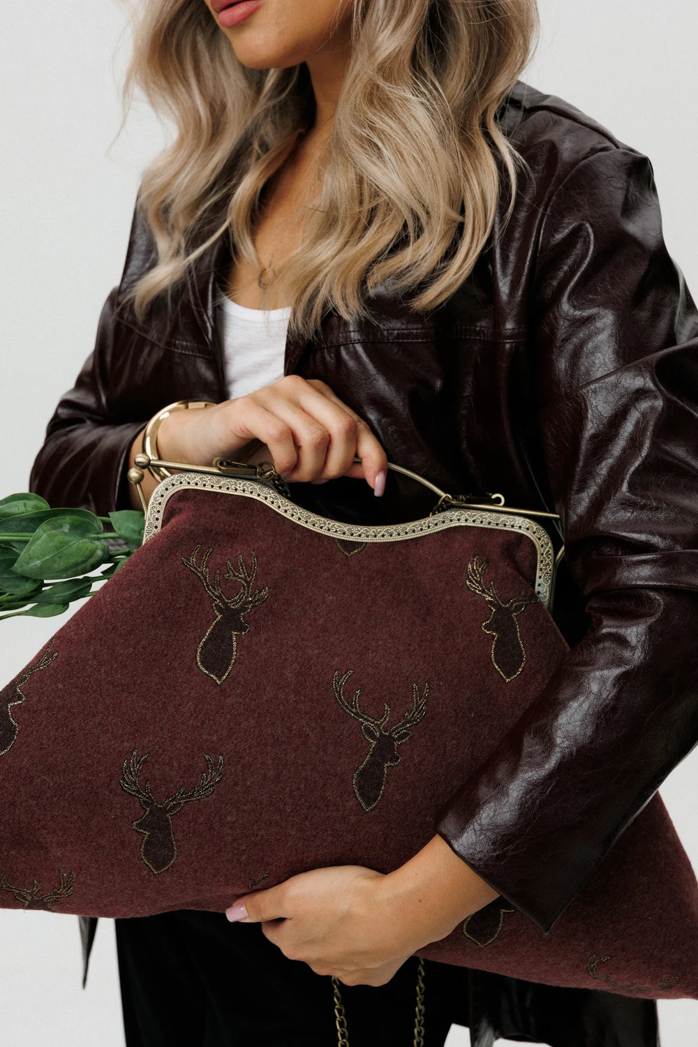 Person holding a brown handbag with deer embroidery against a white background