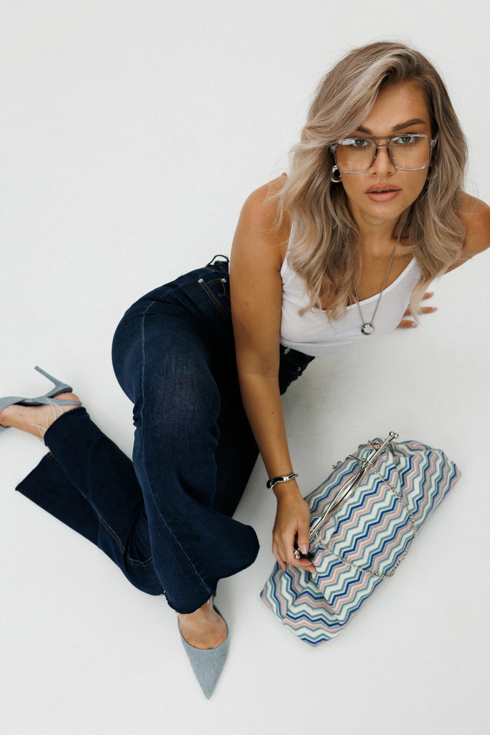 Woman sitting on a white floor with a striped clutch bag