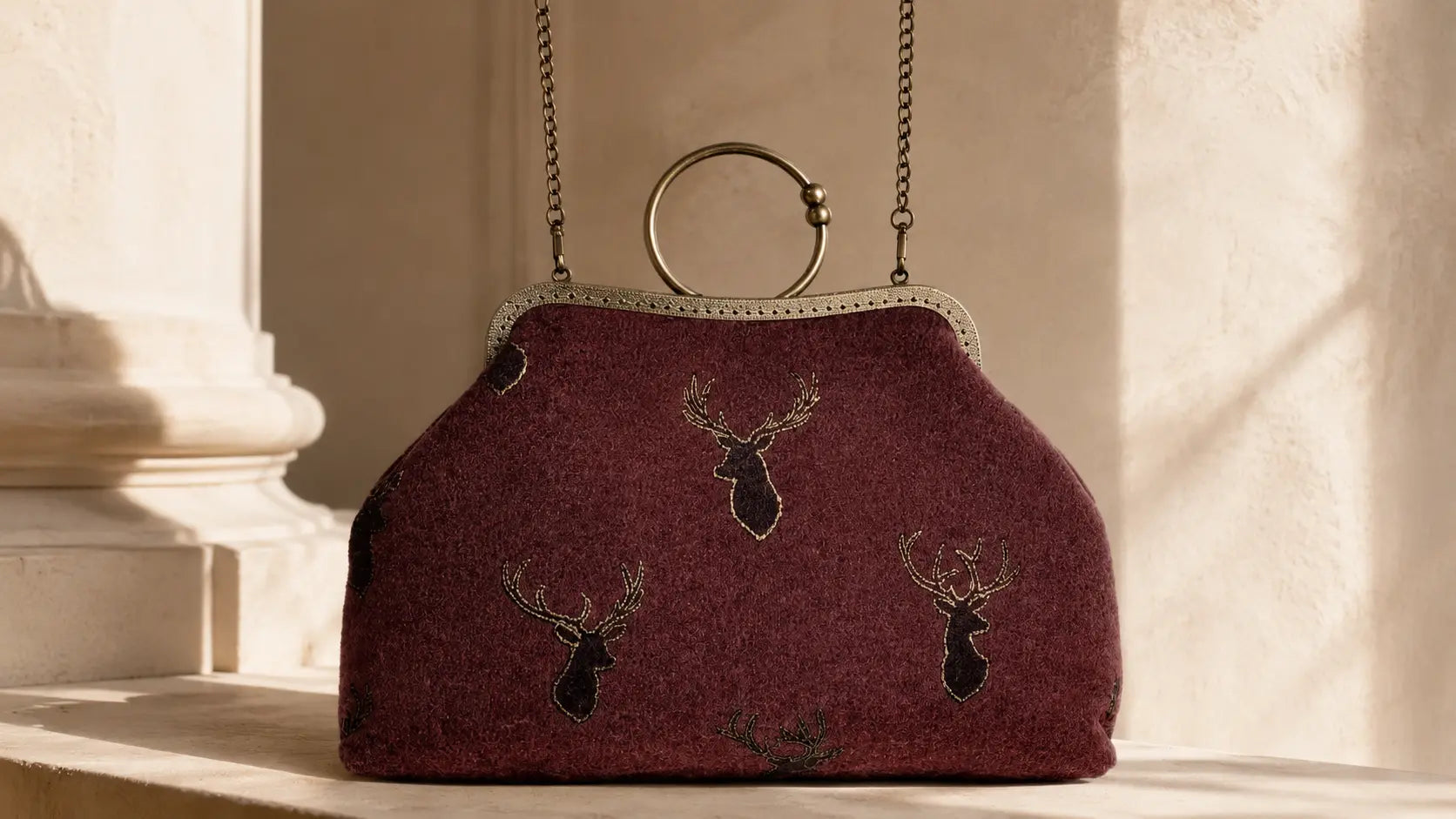 Maroon handbag with deer head designs on a stone surface