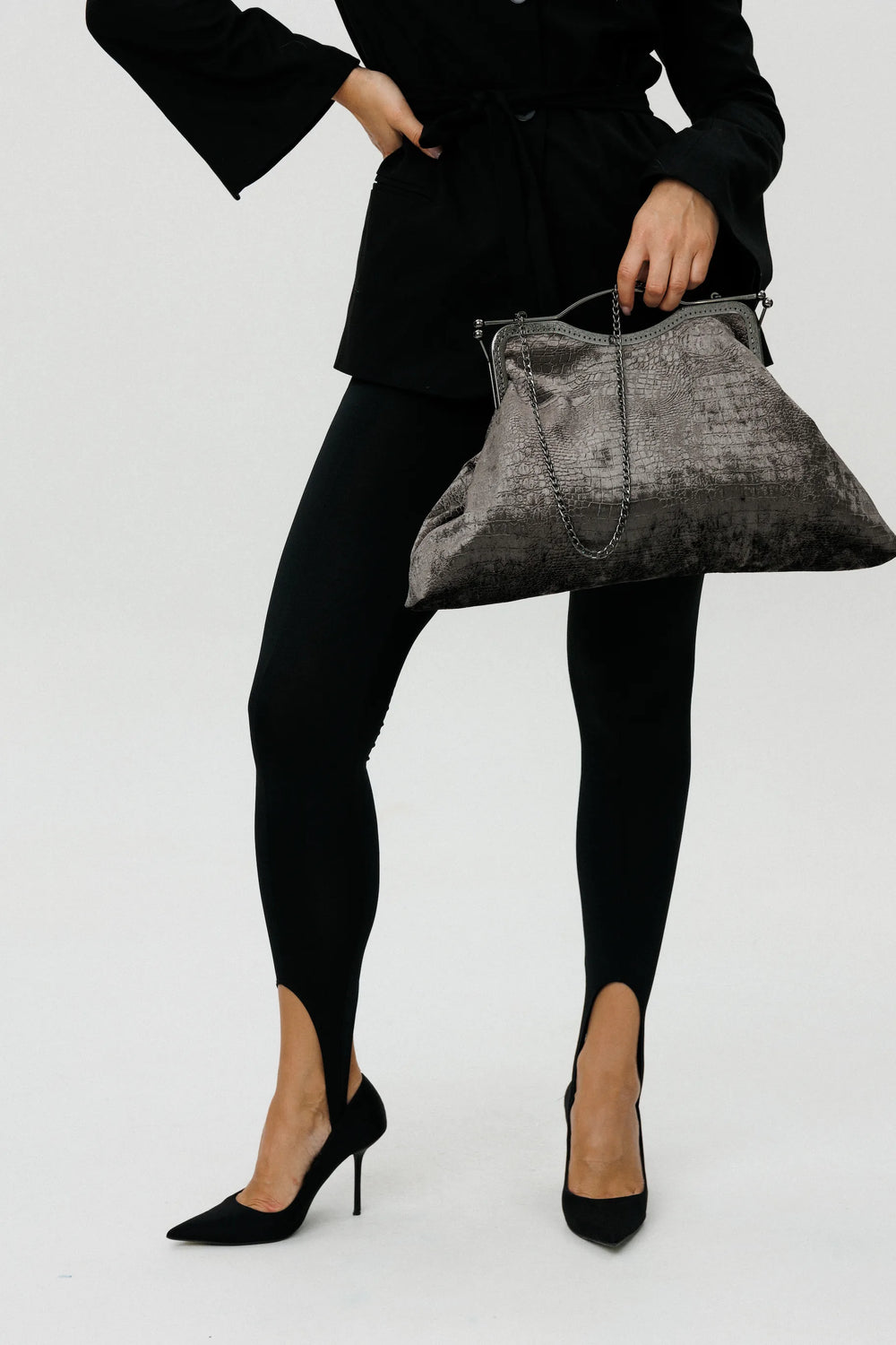 Person wearing a black outfit with a gray handbag on a white background