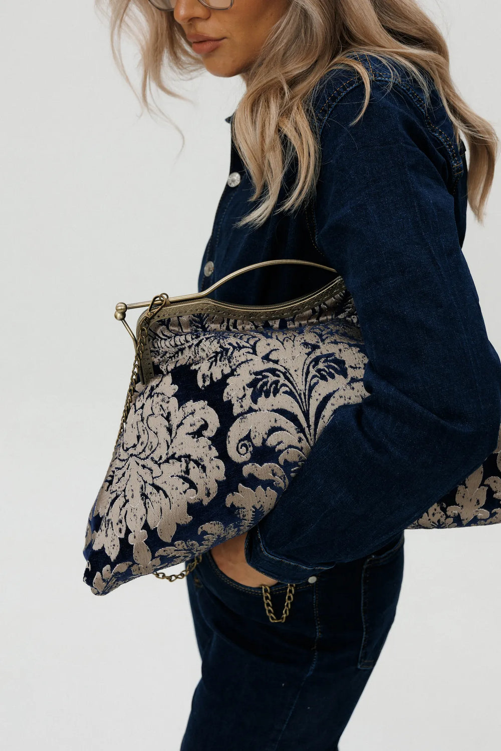 Person holding a decorative clutch bag with intricate patterns on a plain background