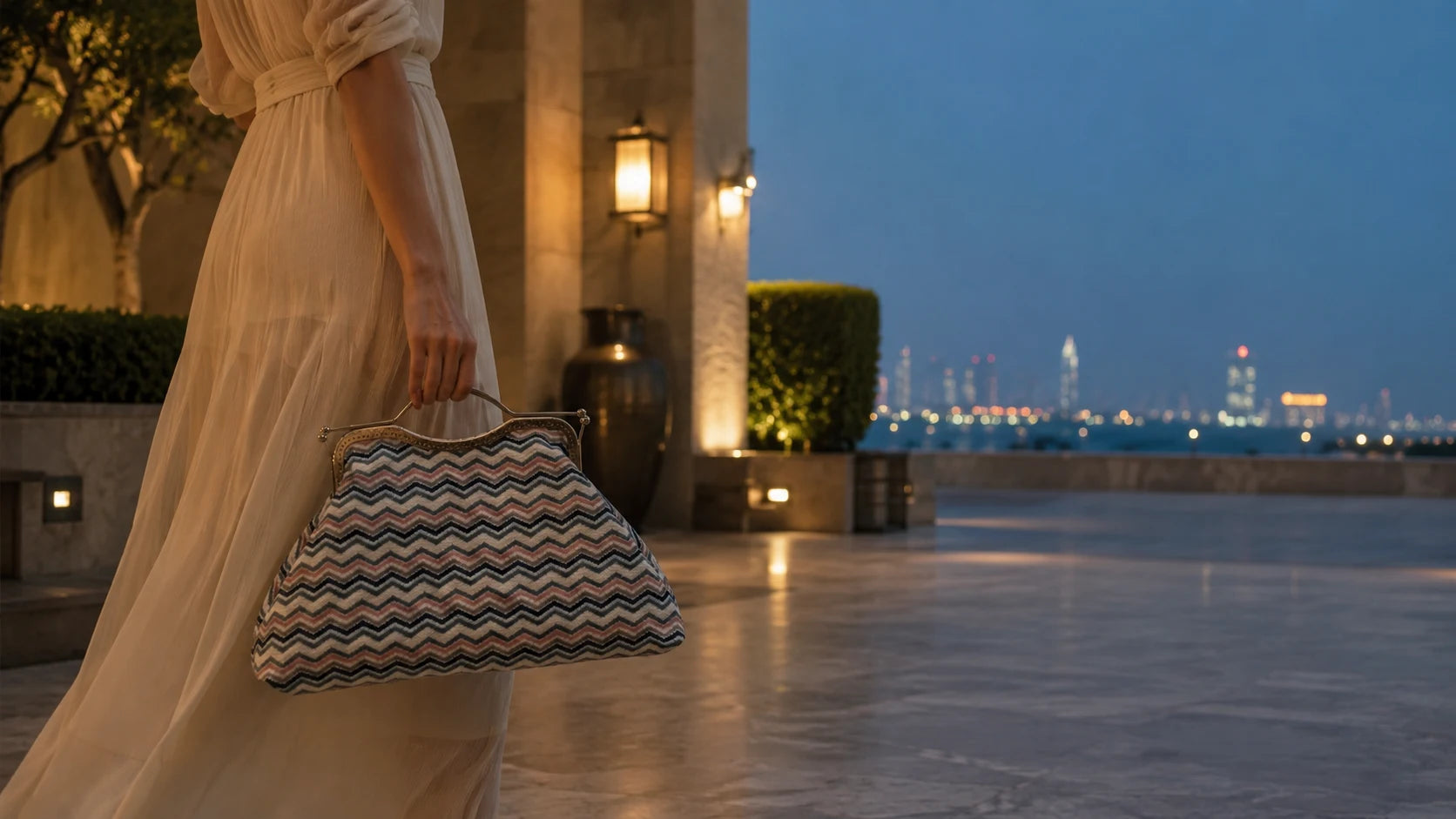 Woman in a long dress holding a patterned handbag with a city skyline in the background.