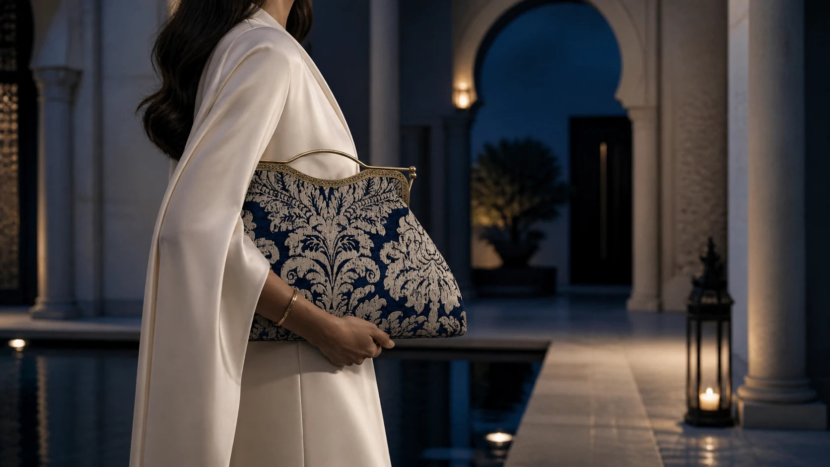 Woman holding a decorative clutch in an elegant outdoor setting with columns and lanterns.